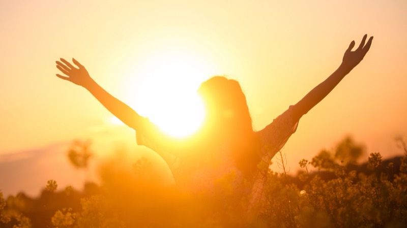 Person breitet im Sonnenaufgang die Arme aus