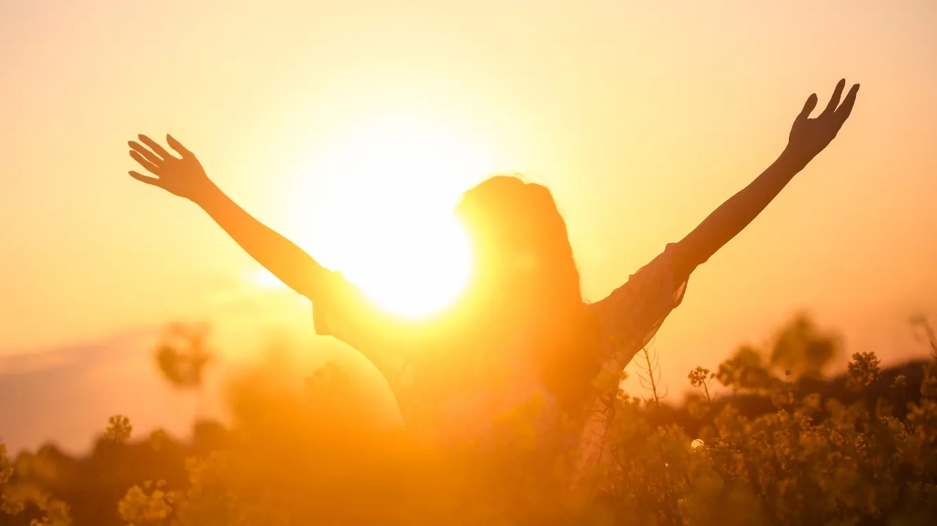 Person breitet im Sonnenaufgang die Arme aus